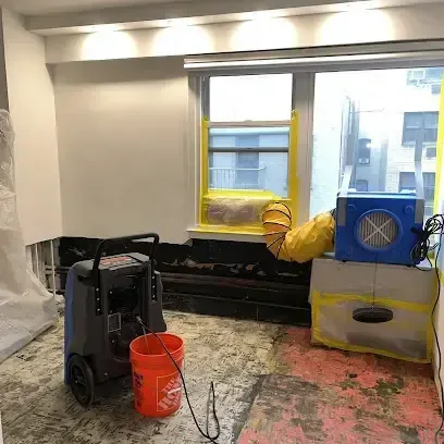 A dehumidifier and an air mover running in an emptied room where the flooring has been pulled up so the subfloor underneath can dry out