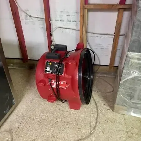 A red air mover and plastic sheeting drying a room with the lower wall opened