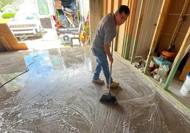 Man pushing muddy floodwater out of a house toward an open garage door