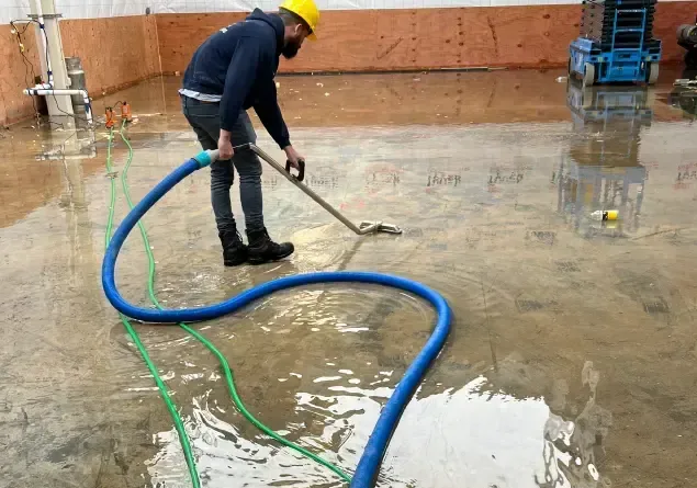 Technician pulling standing water off a flooded floor with a long blue extraction hose